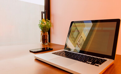Workspace with a laptop and cell phone in an office or at home next to a window on a white desk in warm tones without people