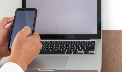 A man's hands handling a cell phone puts together a laptop with a blank screen