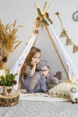 Cute little girl playing with a teddy bear in a wigwam at home.  New Year's decorations.  Happy new year and christmas concept © Наталья Мокрецова