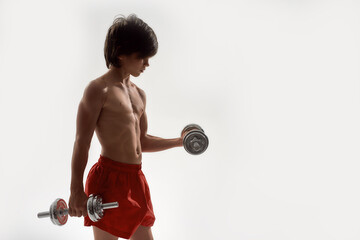 Little sportive boy child with muscular body exercising, showing his muscles, lifting weights while...