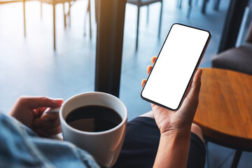 Mockup image of a woman holding mobile phone with blank white desktop screen while drinking coffee