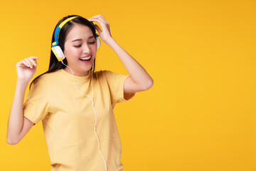 Cheerful enjoy young woman wearing headphones listening to music form smartphone and dancing relax over isolated yellow background. Lifestyle leisure with hobby concept.
