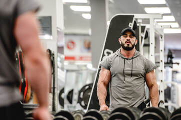 strong young athlete male with beard in sportswear and great physique torso body looking at his reflection in gym mirror posing during workout
