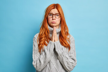 Pleading serious ginger woman upset expression keeps palms pressed together in prayer has...