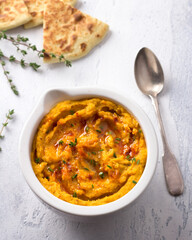 Delicious healthy homemade bean hummus with baked pumpkin, tahina and spices with flat bread on a light blue background, flat lay	