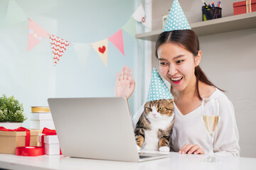 Asian woman and cute cat enjoy celebrating and waving in party via video call conference with...