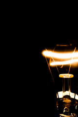 Close up of glowing light bulb on dark background, the bulb at the right edge and copy space for text