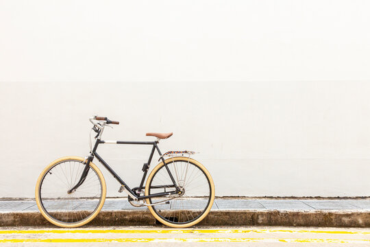 bicycle on the street. Black Vintage Hipster Bicycle With White Tires On A Quiet Street, By A White Wall