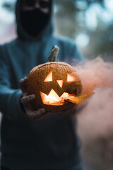 Vertical shot of a man holding a carved pumpkin with an orange smoke - the concept of Halloween
