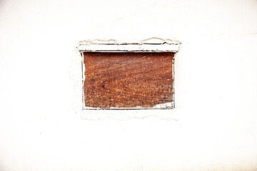 boarded up window with bars on weathered white painted concrete wall