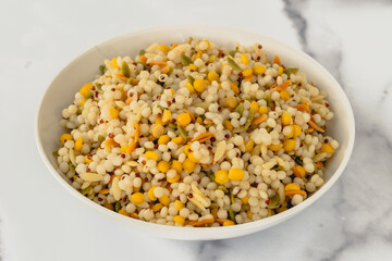 A savory blend of pearled couscous, orzo, baby garbanzo beans, and red quinoa, cooked, and served in a bowl, close up view, marble background