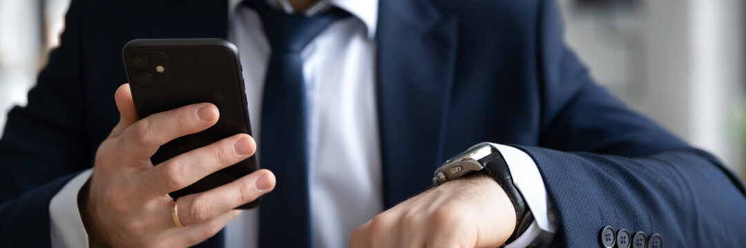 Close up header banner wide image successful businessman in formal suit checking time on wristwatch, arranging working schedule in smartphone application or planning tasks, time management concept.