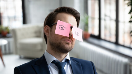 Head shot close up exhausted 30s businessman manager employee sitting in office with paper stickers on eyeglasses, fallen asleep after hard working overload day in office, fatigue burnout concept.