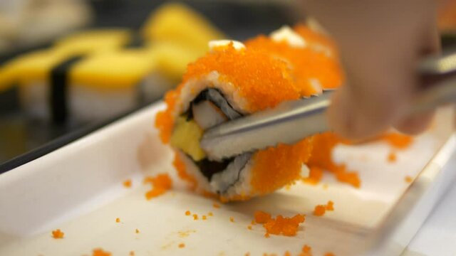 Close-up of picking up sushi roll topped with tobiko using tongs