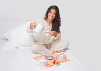 Obraz na płótnie Canvas Spanish attractive brunette woman sitting on a bed having a cup of coffee or tea