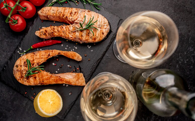 Dinner for two. Grilled salmon steaks, bottle of wine and glasses on stone background. View from above