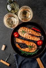 Dinner for two. Salmon steaks in a grill pan, a bottle of white wine and glasses on a stone background.
View from above