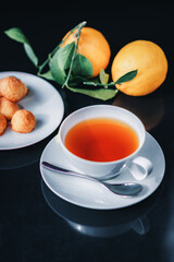 White glass cup with black, red tea with lemon on a dark glass table.