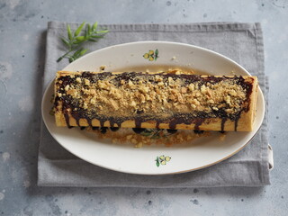 Pastry roll filled with apple jam, poured with chocolate icing and sprinkles, on a gray wooden background.Homemade baked goods.