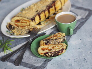 Pieces of pastry roll with apple jam filling, poured with chocolate icing and sprinkles, on a gray wooden background. Homemade pastries and a cup of coffee for breakfast.
