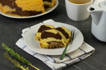 Marmer Cake or marbel Cake on white ceramic, served with a cup of coffee. Black marble background. 