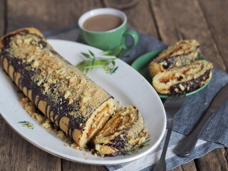 Homemade pastries and a cup of coffee for breakfast. Pieces of pastry roll stuffed with apple jam, sprinkled with chocolate icing and sprinkles, on a wooden background.
