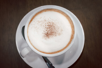 Frothy hot coffee and stainless steel spoon are placed on the table in the coffee shop.