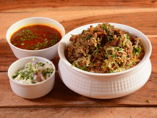 Traditional Hyderabadi Chicken dum Biryani made of Basmati rice cooked with masala spices, served with Onion raita and Salan, selective focus