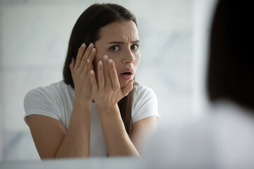 Oh god, a pimple. Anxious worried girl teenager or millennial woman watching herself in big mirror...