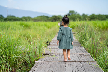 little girl walking on wooden bridge at grass field.