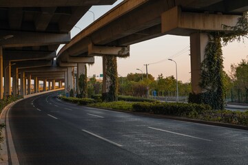 Urban road under overpass bridge at sunset.