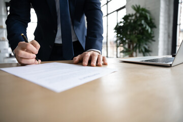 Close up young male ceo executive manager standing near table, doing company paperwork, putting...