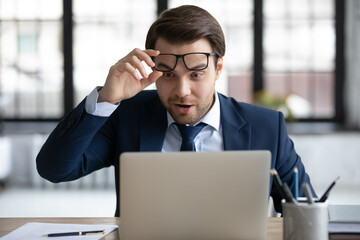 Surprised lucky 30s male ceo manager employee in formal wear can't believe his eyes, looking at...