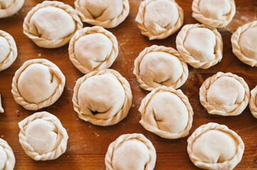 Fototapeta na wymiar pile of small homemade uncooked dumplings with meat on kitchen table. national traditional Russian cuisine. do it yourself. top view, flat lay