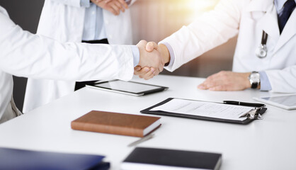 Unknown doctors are shaking their hands as agreement about patient's diagnosis in a sunny cabinet, close-up. Medical help, insurance in health care