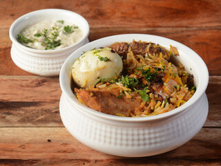 Traditional Hyderabadi Chicken dum Biryani made of Basmati rice cooked with masala spices, served with boiled egg and Onion raita, selective focus