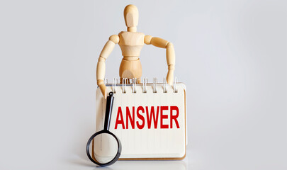 Wooden man shows with a hand to white notepad with text ANSWER