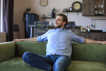 Handsome young business man is looking relaxed while sitting on the couch at home.