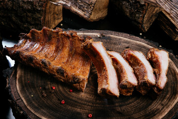 Smoked pork ribs laid out on a wooden brown background. Tree stump and firewood