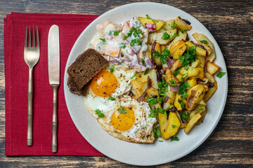Ukrainian food, fried potatoes with onions, eggs, vegetable salad, black bread on wooden background