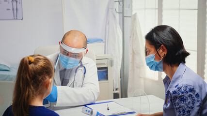 Pediatrician with protection mask using tabet in medical office. Physician specialist in medicine providing health care services consultation treatment examination in hospital cabinet during covid-19