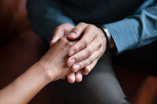 Hand in hands. Close up of young man husband boyfriend holding hand of beloved mixed race woman wife girlfriend comforting supporting in grief, asking forgiveness, apologizing after family argument