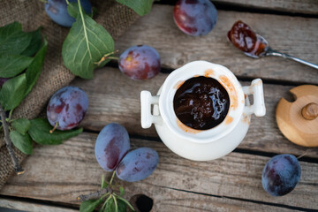 plum jam in a white ceramic pot on an aged wooden background, fresh plums near