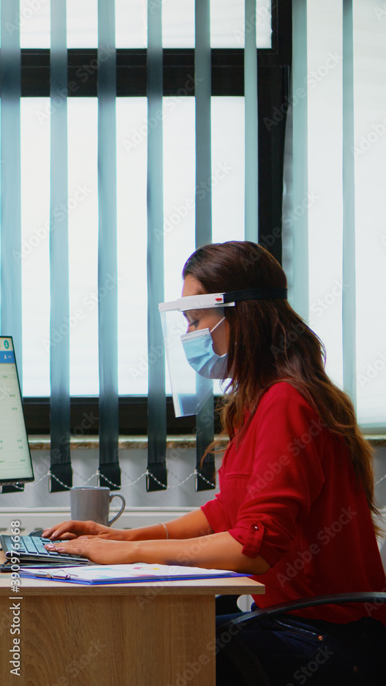 Poster people with mask and visor working in new normal office checking reports and writing on computer. co