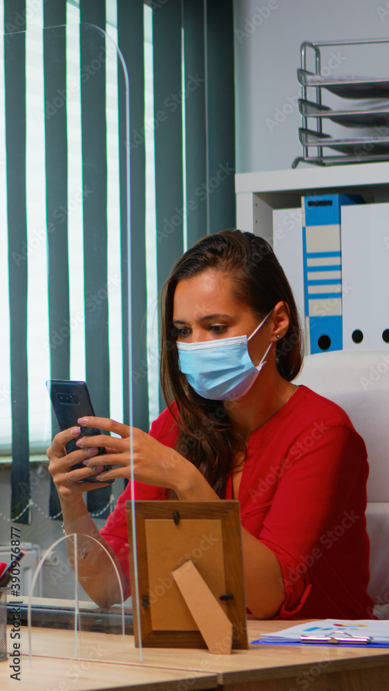 Poster woman with protective mask typing on phone while colleague working using clipboard respecting social
