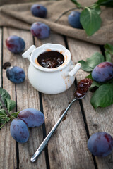 plum jam in a white ceramic pot on an aged wooden background, fresh plums near