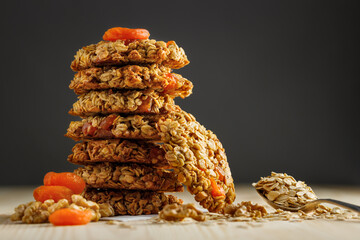 Sweet oatmeal cookies with nuts, dried apricots and a spoonful of oatmeal on a wooden table.