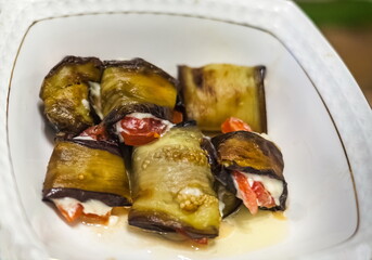 Baked pieces of red fish with cheese wrapped in a plate of eggplant on a white platter close-up