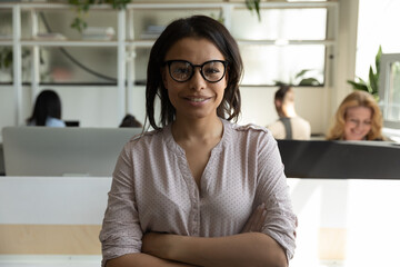 Successful career. Portrait of confident biracial female team leader expert executive worker standing on workplace in open space office with arms crossed on chest looking at camera with happy smile - Powered by Adobe