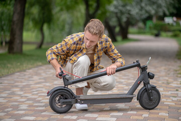 Man in checkered shirt looking involved while fixing push scooter